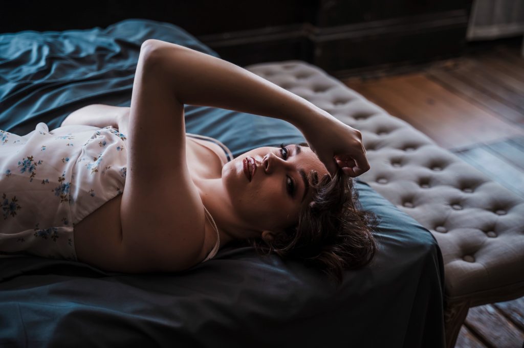 Woman in floral lace lingerie reclining on a dark tufted bed during a moody boudoir photography session in Columbus Ohio