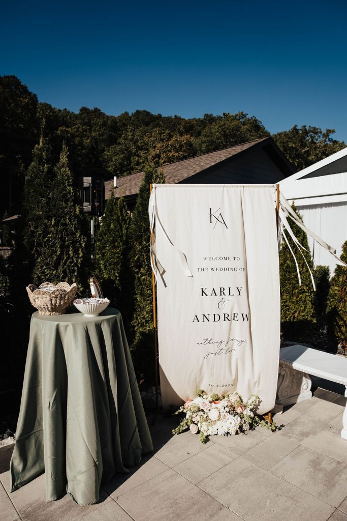 Fabric wedding welcome sign for Karly and Andrew beside a sage green cocktail table at Knotting Hills venue, photographed by Blue Willow.