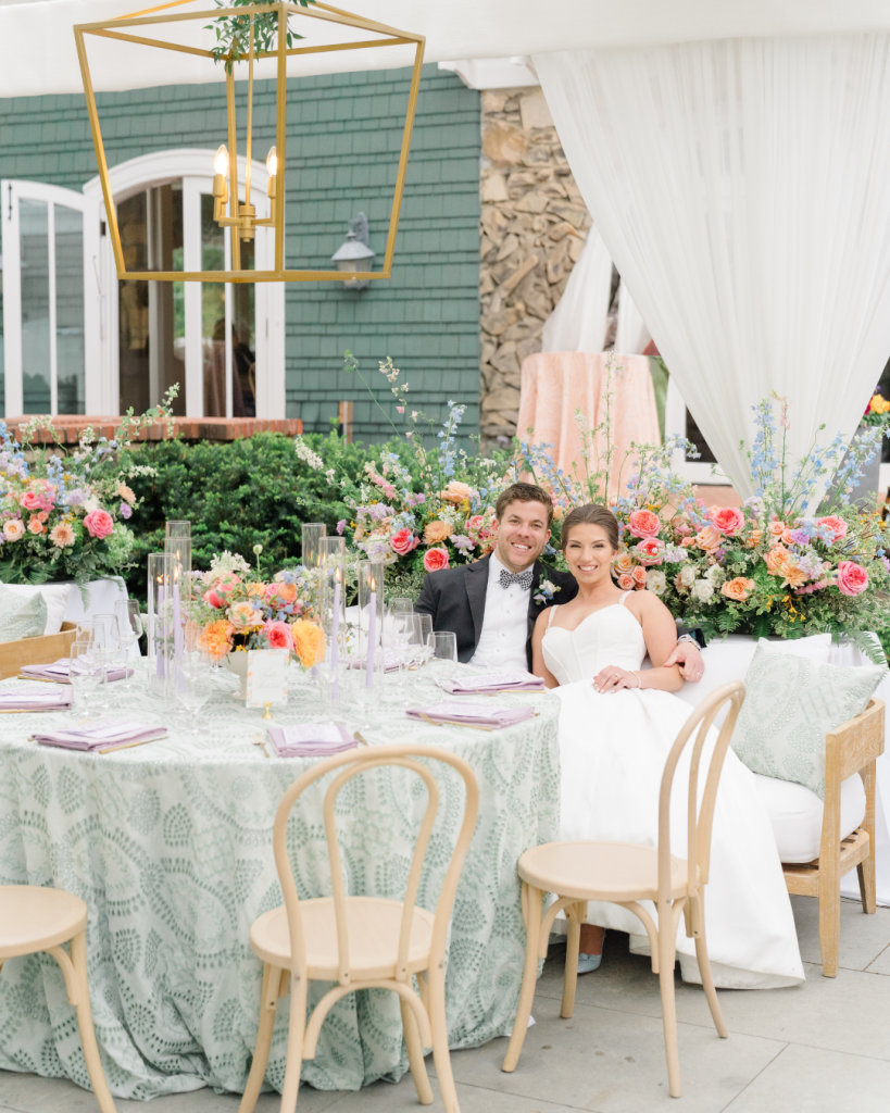 Bride and groom seated together in a floral filled reception lounge at The VanLandingham Estate in Charlotte, NC surrounded by colorful spring blooms and elegant garden party décor.
