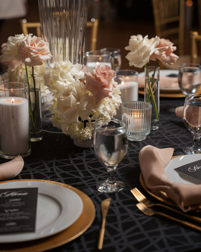 Candlelit wedding reception table at The Mint Museum in Charlotte featuring blush roses, white hydrangeas, gold place settings, and elegant tablescape design.
