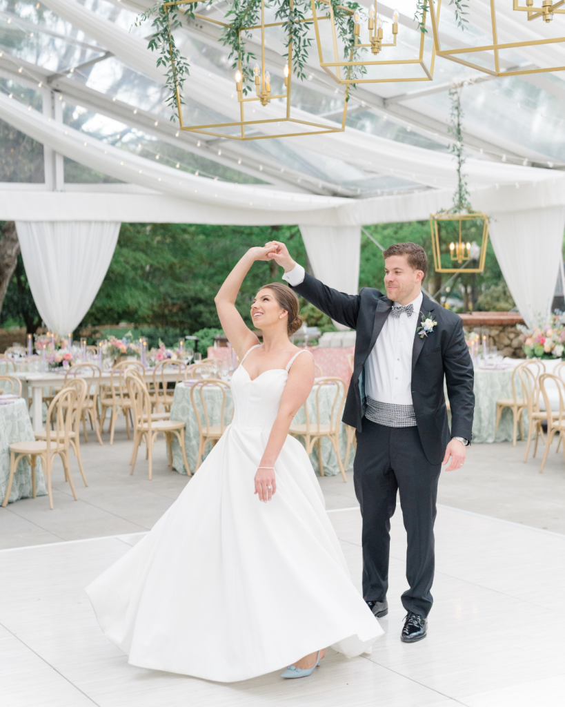 Bride and groom sharing their first dance beneath greenery wrapped lanterns and a clear top reception tent in Charlotte, North Carolina.