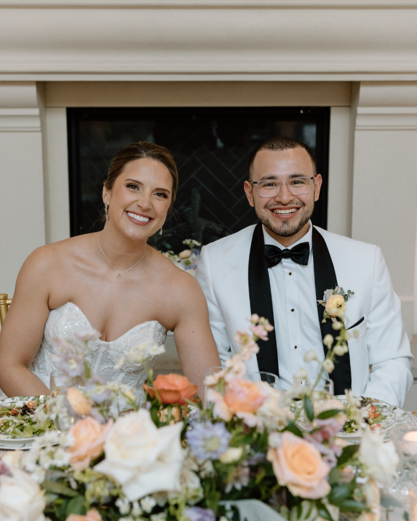 husband and wife smiling at wedding reception sitting at sweetheart table