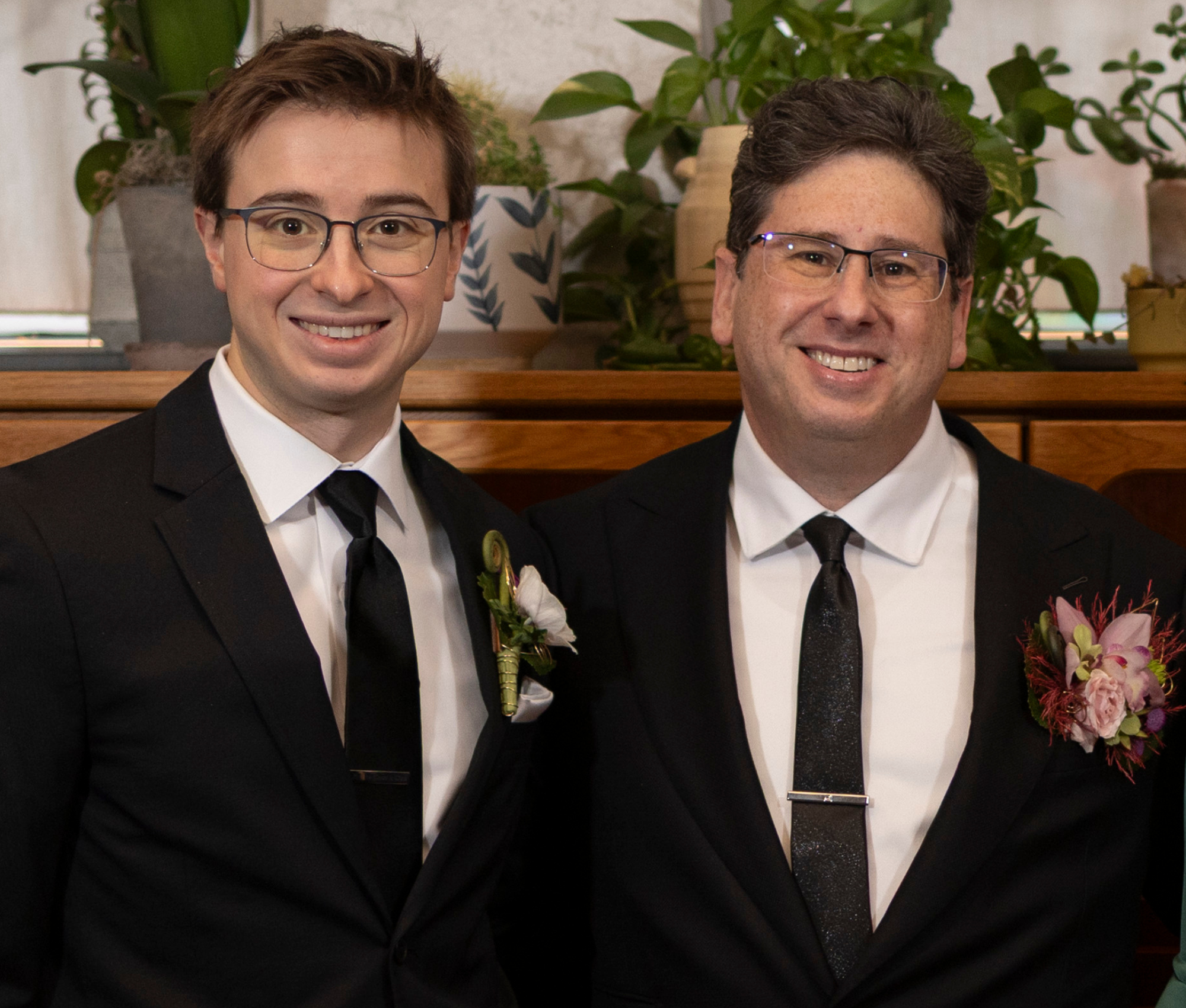 A groom and groomsman wearing custom black wedding suits tailored by Young & Squire, photographed at their wedding celebration.