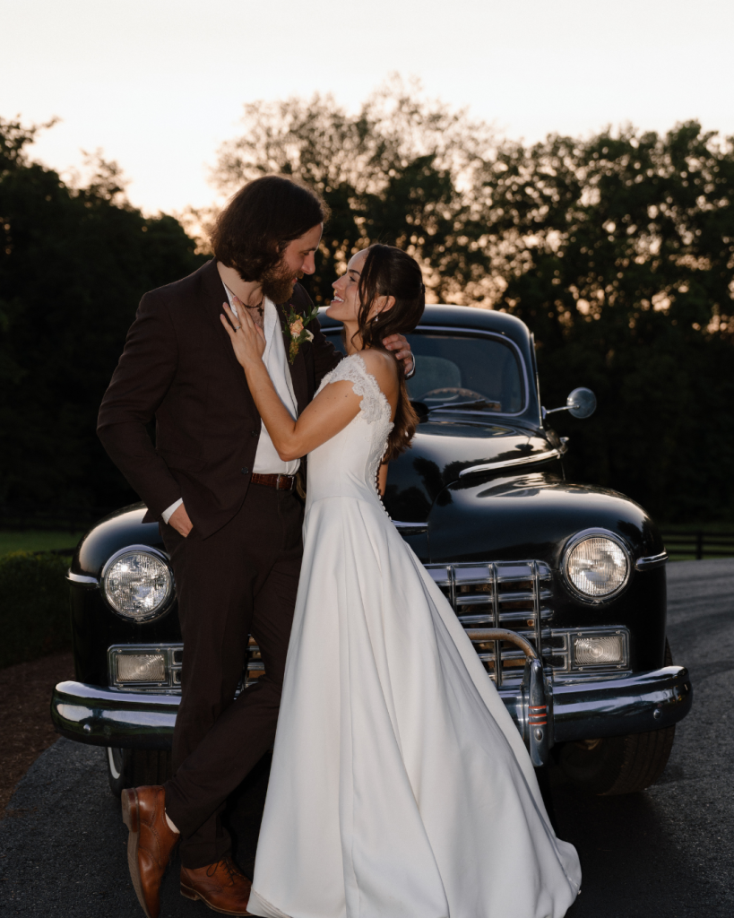 bride and groom kissing in front of vintage car at dusk