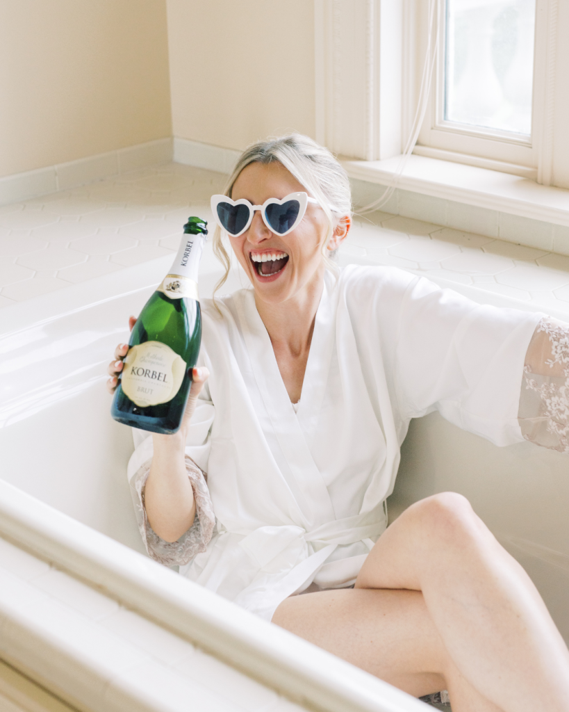 bride wearing heart sunglasses with bottle of champagne during get ready with bridesmaid