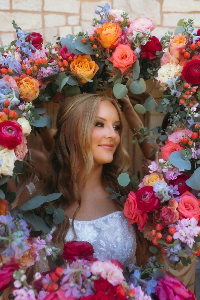 Profile of a bride framed by a lush, colorful floral arch at Silver Oaks Chateau, by Mad Land Photography.