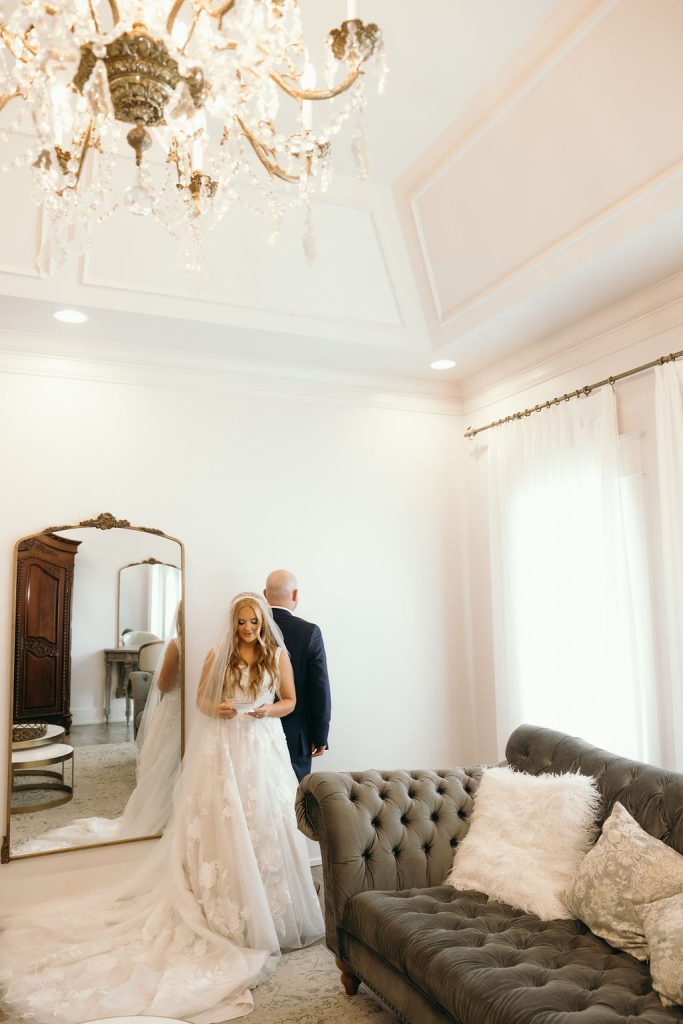 Bride reading a letter while standing back-to-back with the groom in a bridal suite at Silver Oaks Chateau, by Mad Land Photography.