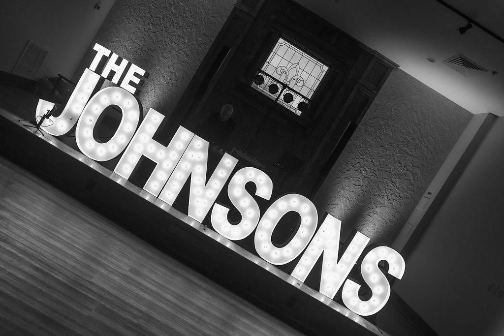 Black and white photo of large marquee letters spelling "THE JOHNSONS" lit up on a reception stage from Alpha-Lit STL.