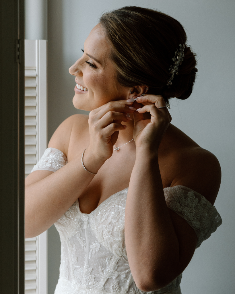 bride looking out the window while putting on bridal earrings during getting ready portrait before wedding ceremony in northern virginia