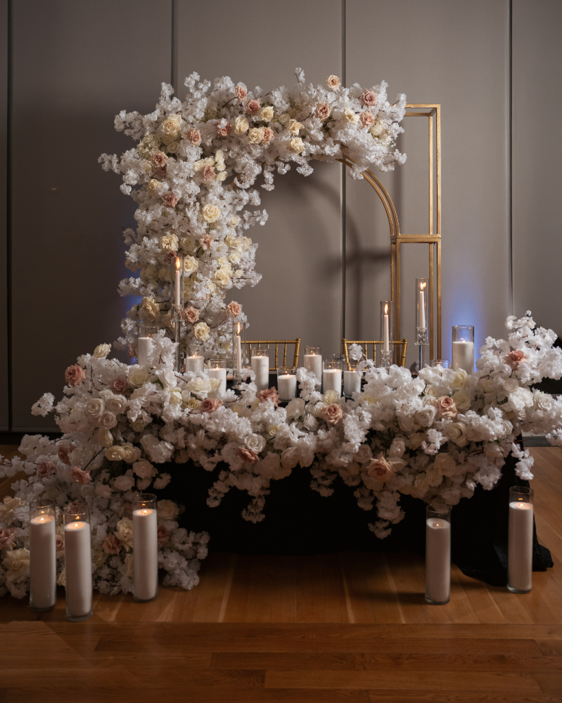 Luxury floral installation featuring blush and ivory roses, white blossoms, gold accents, and candlelight at a Charlotte wedding reception.