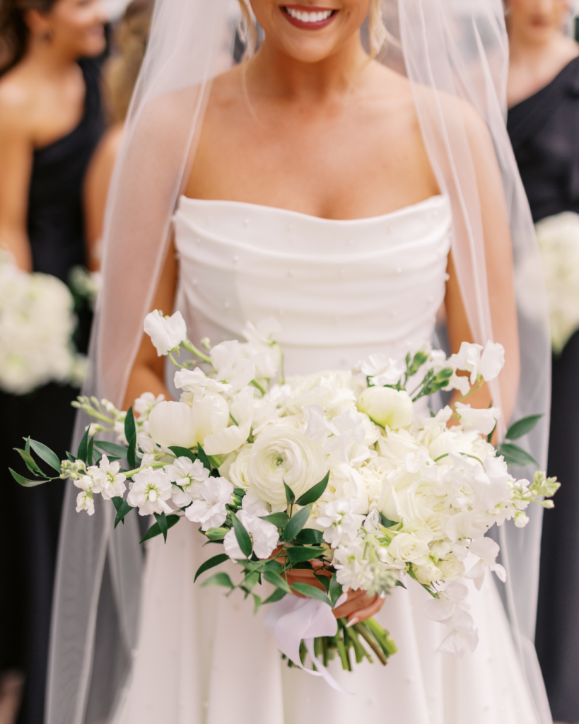 Close up of bride's white floral bouquet featuring roses, hydrangea, ranunculus, and sweet peas by Florallori.
