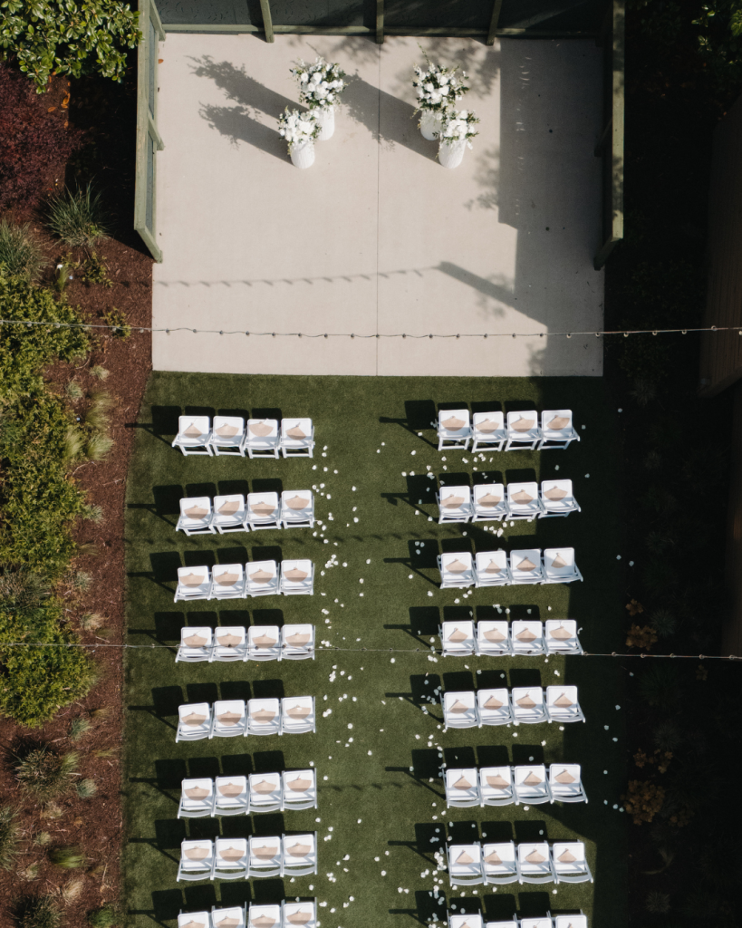 Aerial view of an outdoor wedding ceremony setup featuring white chairs, rose petals, and floral arrangements at The Ruth in Charlotte, North Carolina.