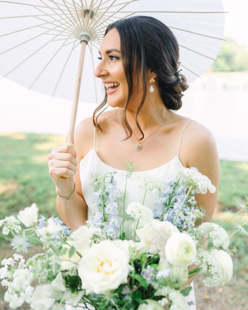 Bride holding a white parasol and loose garden bouquet of white and pale blue flowers at Kent Island Resort on Maryland's Eastern Shore