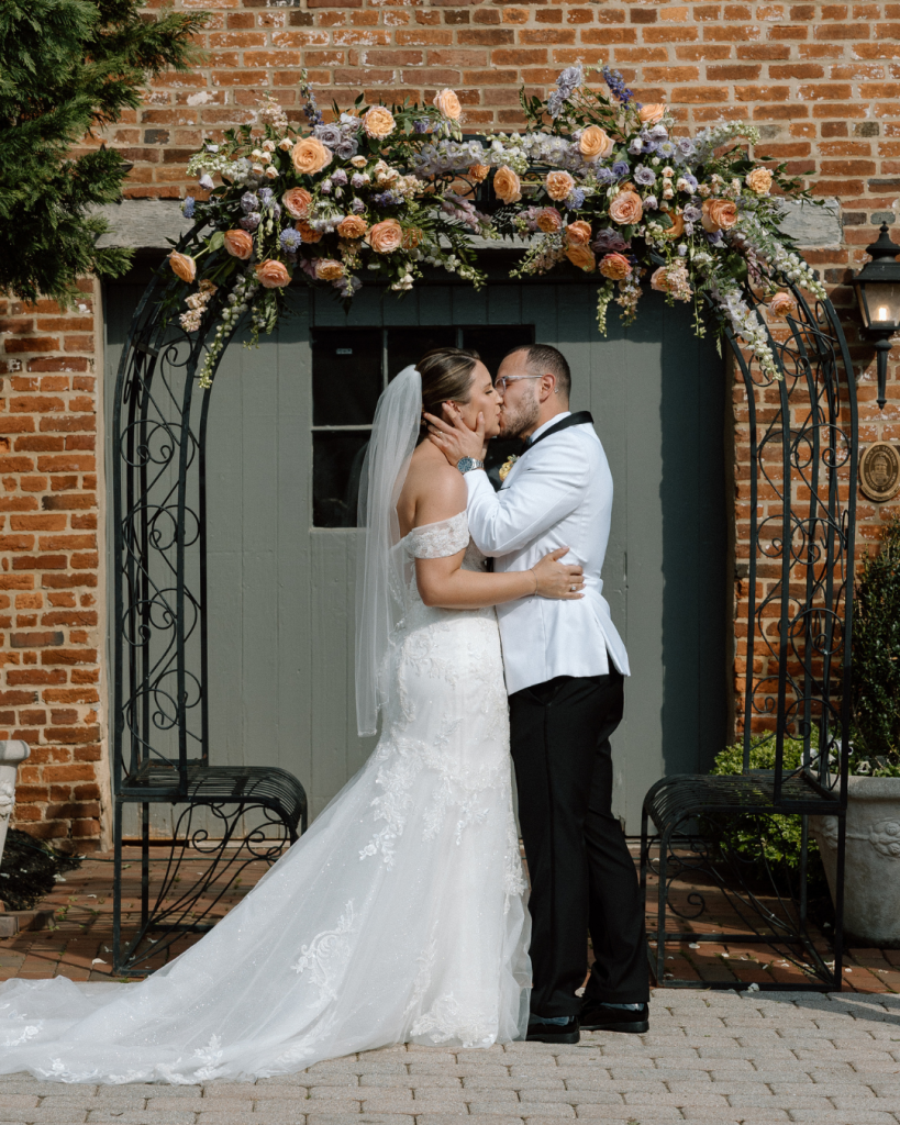 Husband and Wife sharing first kiss under flower filled wedding altar