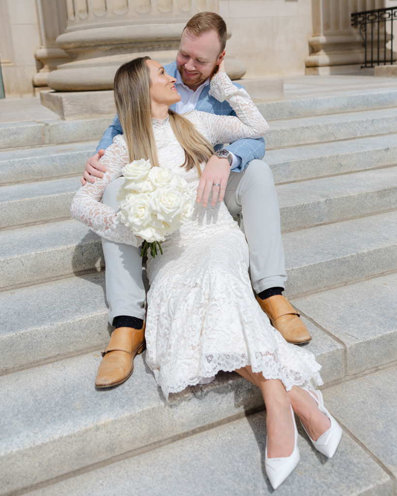 Audrey and Steve sit together on the courthouse steps in Charlotte, NC sharing a quiet moment after their wedding ceremony while holding a bouquet of white roses.