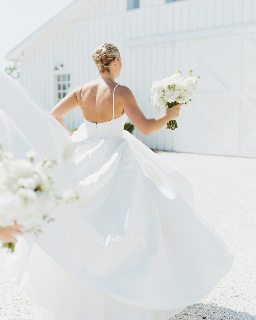 Bride twirling in her modern satin wedding gown outside a white barn during an elegant Maryland Eastern Shore wedding.