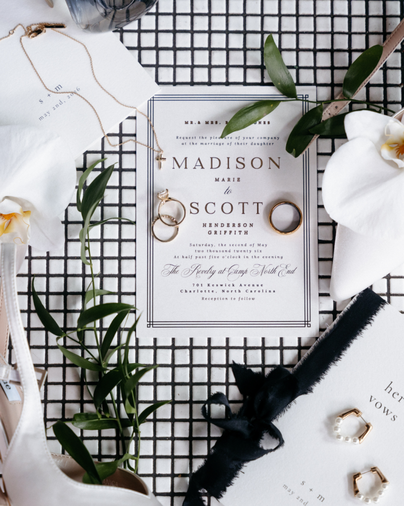 Wedding invitation suite featuring black and white stationery, wedding rings, greenery, ribbon, and bridal accessories.