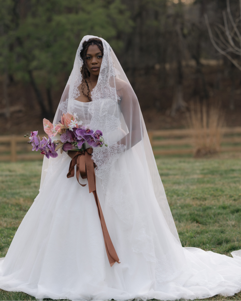 Bride portrait in a lace trimmed veil holding a bouquet of lavender orchids, blush anthuriums, and pink florals at The Lumen House wedding venue.