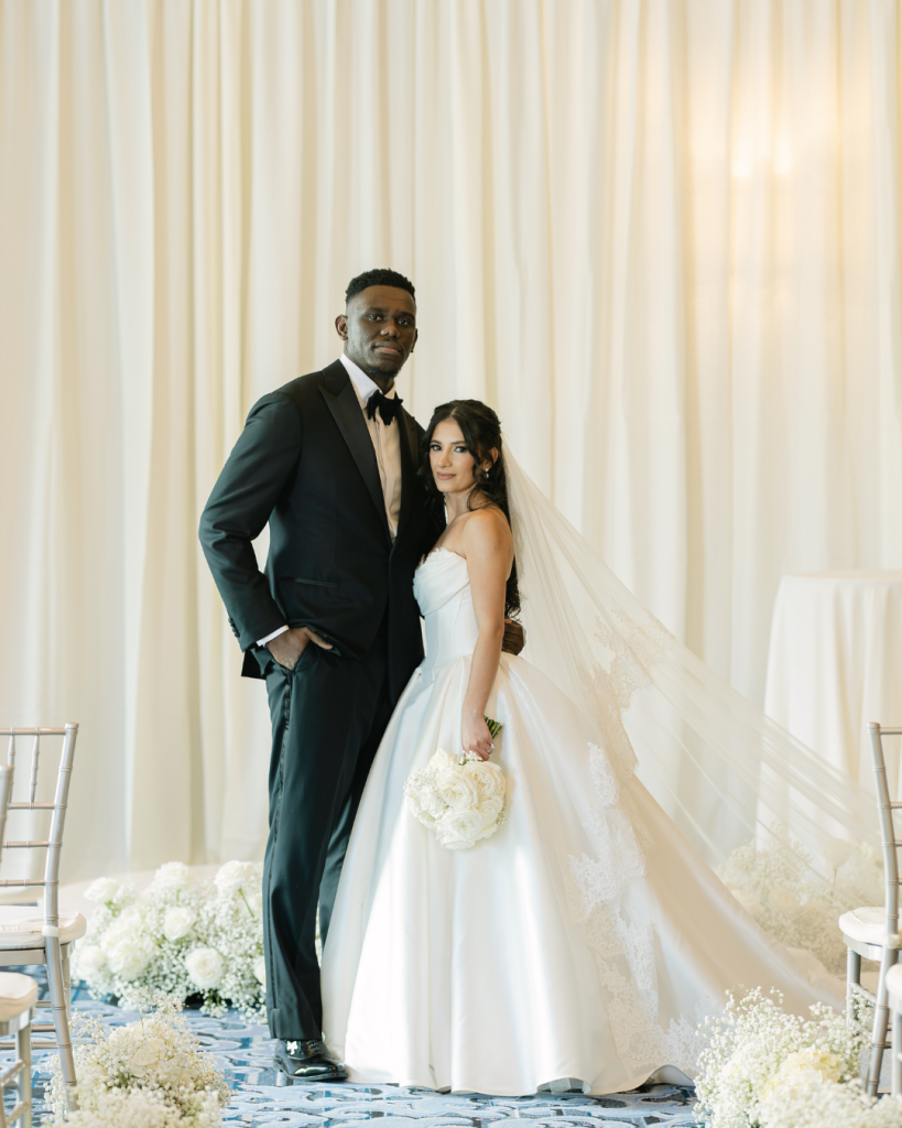Bride and groom pose beneath soft white draping surrounded by floral arrangements from Little Dove Floral during their wedding reception in Charlotte.