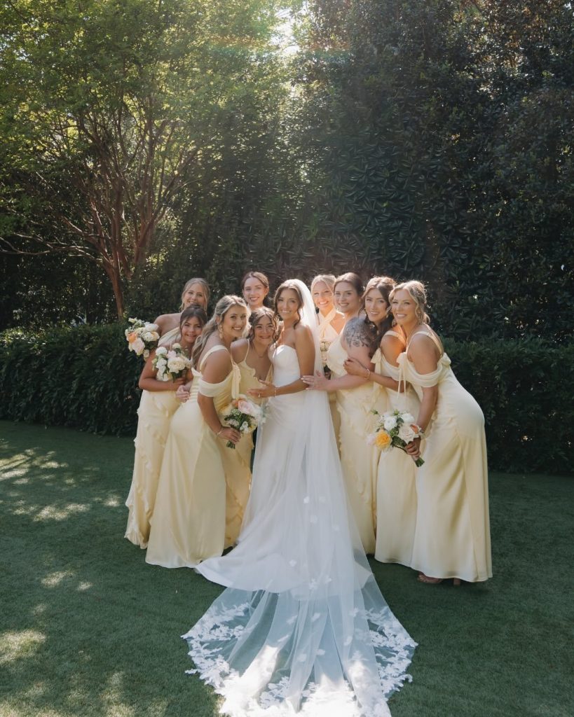 Bridesmaids in yellow silk dresses surrounding a bride with a long lace-trimmed veil for wedding party inspiration.