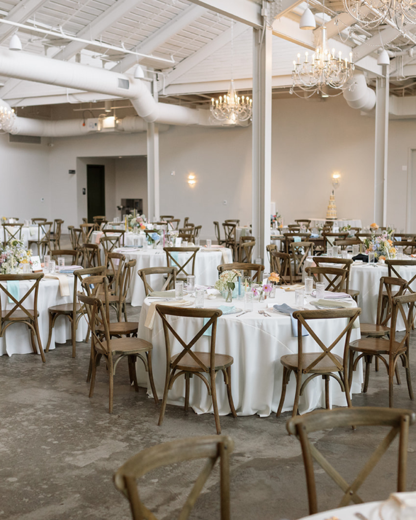 Wide view of The Casey reception space showcasing round guest tables, chandeliers, floral centerpieces, and wedding reception decor in Charlotte, NC.