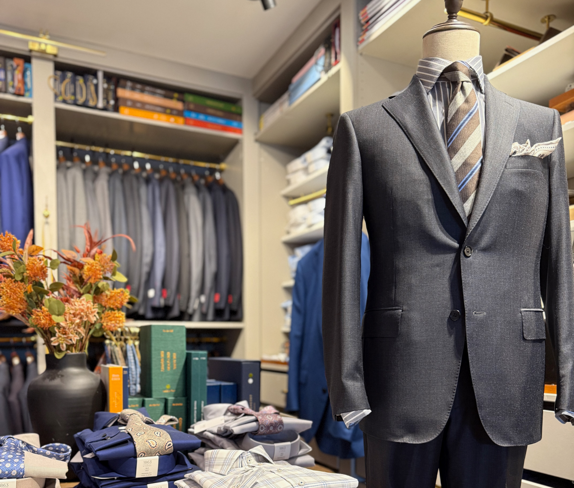 Custom charcoal suit displayed on a mannequin inside the Young & Squire menswear studio in Greenville, Delaware, surrounded by luxury fabrics, accessories, and bespoke tailoring details.