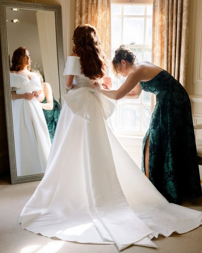 bridesmaid helping bride put on final touches of wedding dress during getting ready morning