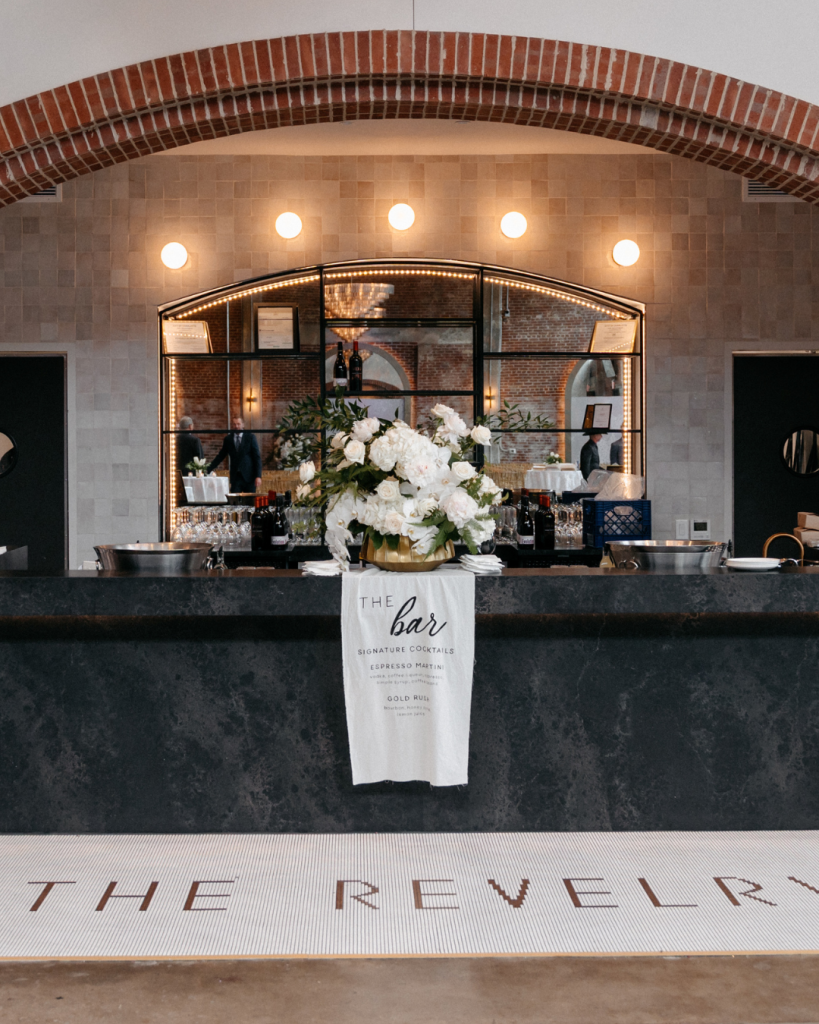 Signature cocktail display with white floral centerpiece at The Revelry wedding reception in Charlotte, North Carolina.