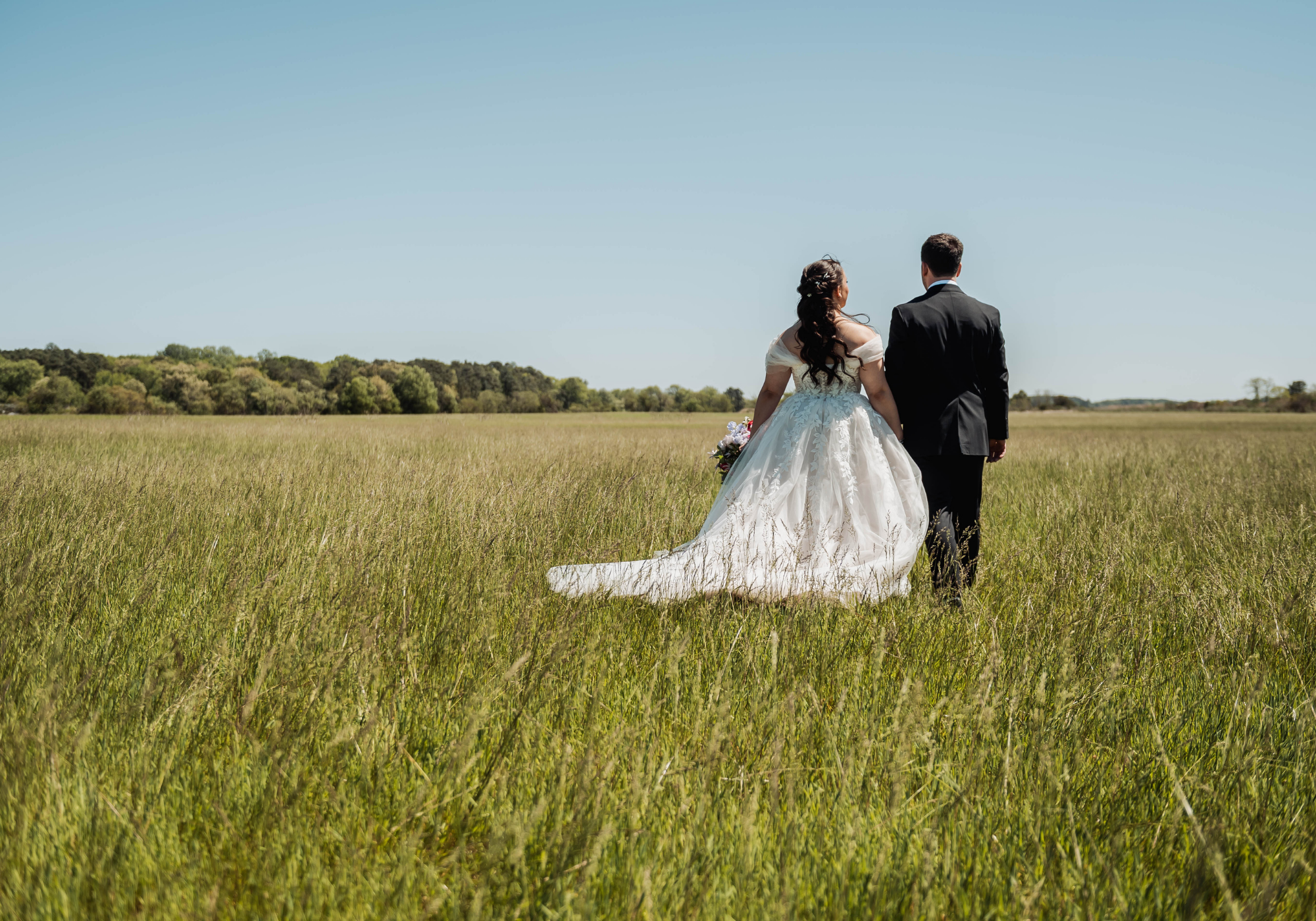 Bride and groom walking hand in hand through an open field at Kent Island Resort on Maryland’s Eastern Shore.