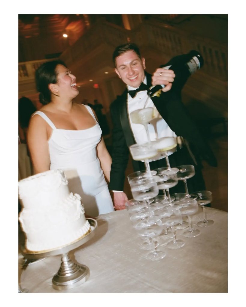 bride and groom laughing while pouring champagne tower at wedding reception