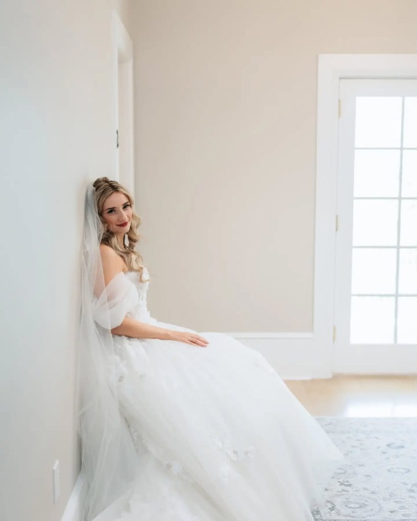 bride sitting down relaxing looking at camera in wedding dress at indoor wedding getting ready space in northern virginia