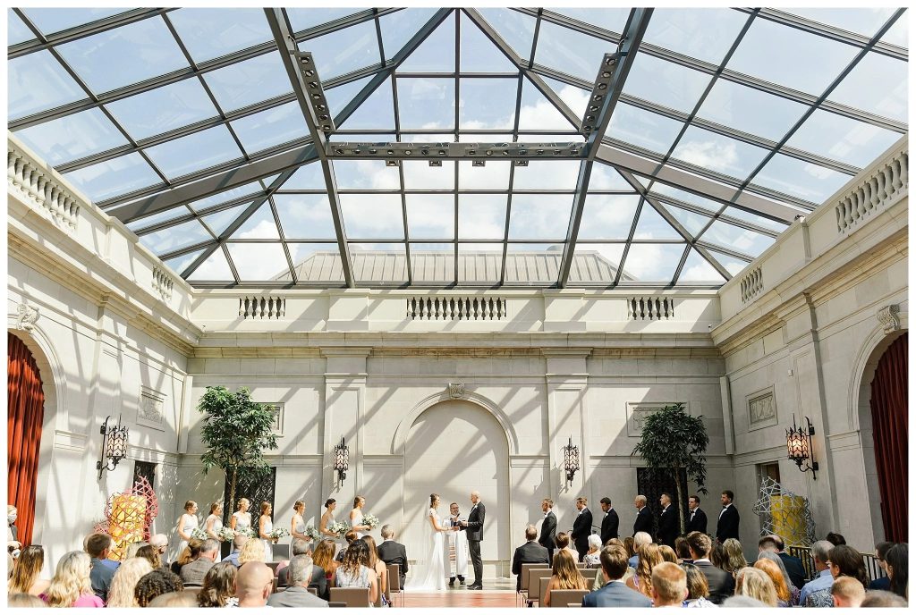 Wedding ceremony at the Columbus Museum of Art in downtown Columbus, Ohio, featuring a bright glass atrium, contemporary artwork, and guests gathered as the couple exchanges vows beneath soaring architecture.