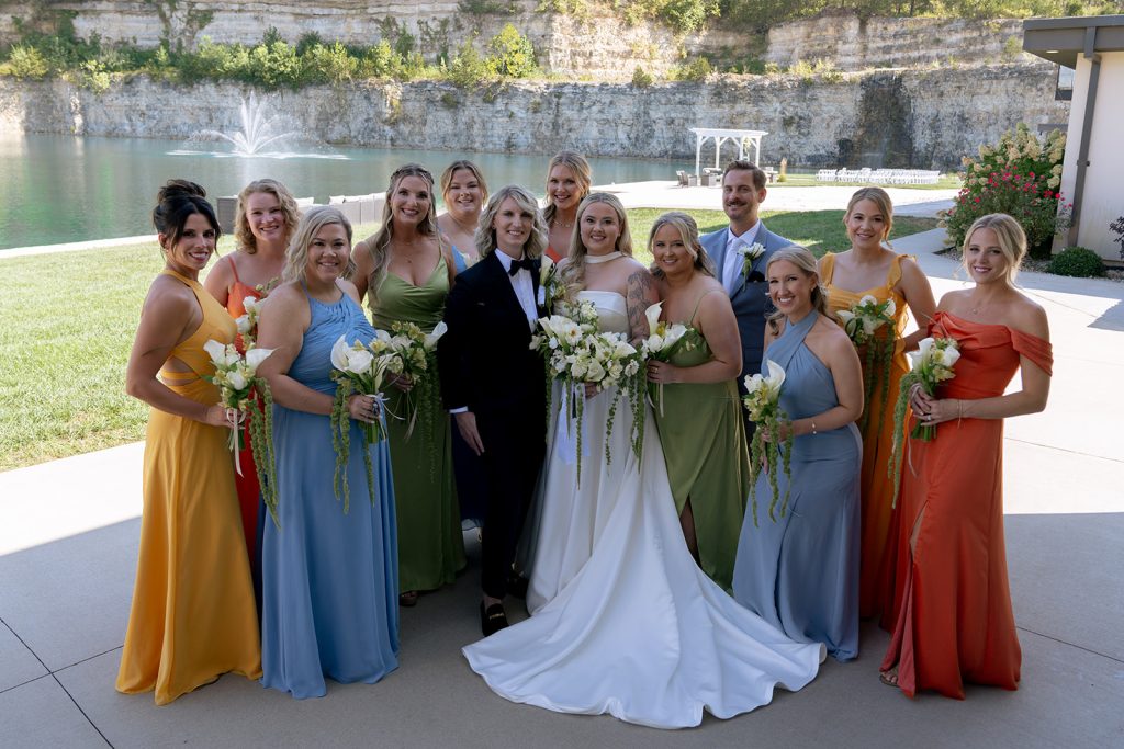 Brides standing with their wedding party in gem colored dresses holding florals by Cultivated Blooms.