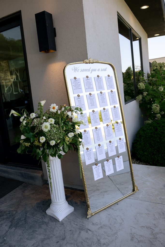 Seating chart on large gold accent mirror framed with a grant floral arrangement by Cultivated Blooms.