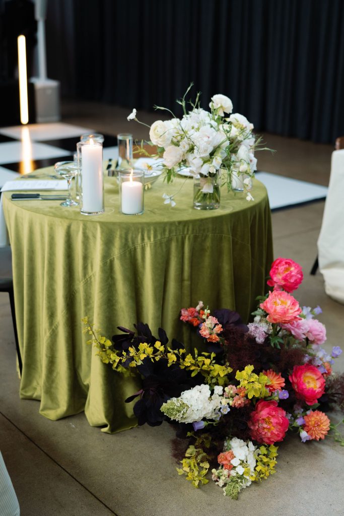 Sweetheart table with sage green table cloth adorned with bright floral arrangement.