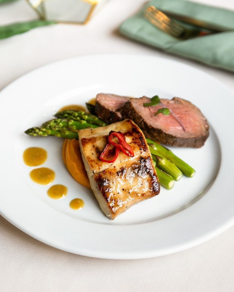 Plated wedding entrée by Emilio’s Catering in Columbus, Ohio featuring sliced beef tenderloin, glazed fish, fresh asparagus, sweet potato purée, and sauce accents on a white dinner plate at a wedding reception.