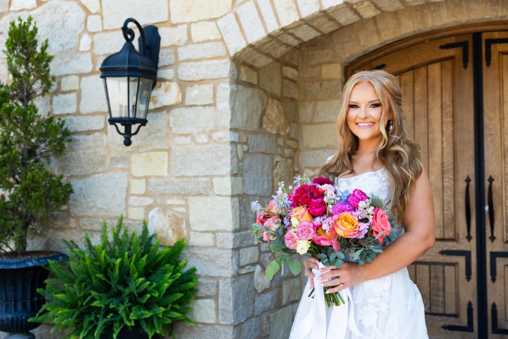 Close-up of a smiling bride holding a vibrant pink and orange bouquet at Silver Oaks Chateau, by Mad Land Photography.
