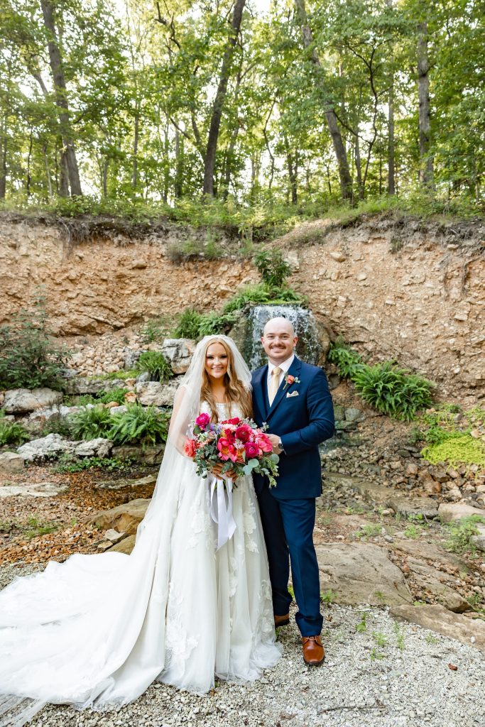 Bride in a Mia Grace Bridal gown and groom posing by a waterfall at Silver Oaks Chateau, by Mad Land Photography.