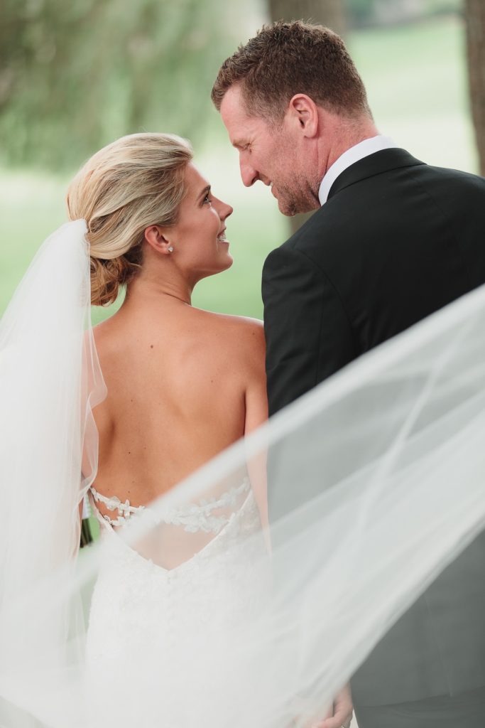 Close wedding portrait of a smiling bride and groom framed by her flowing veil.