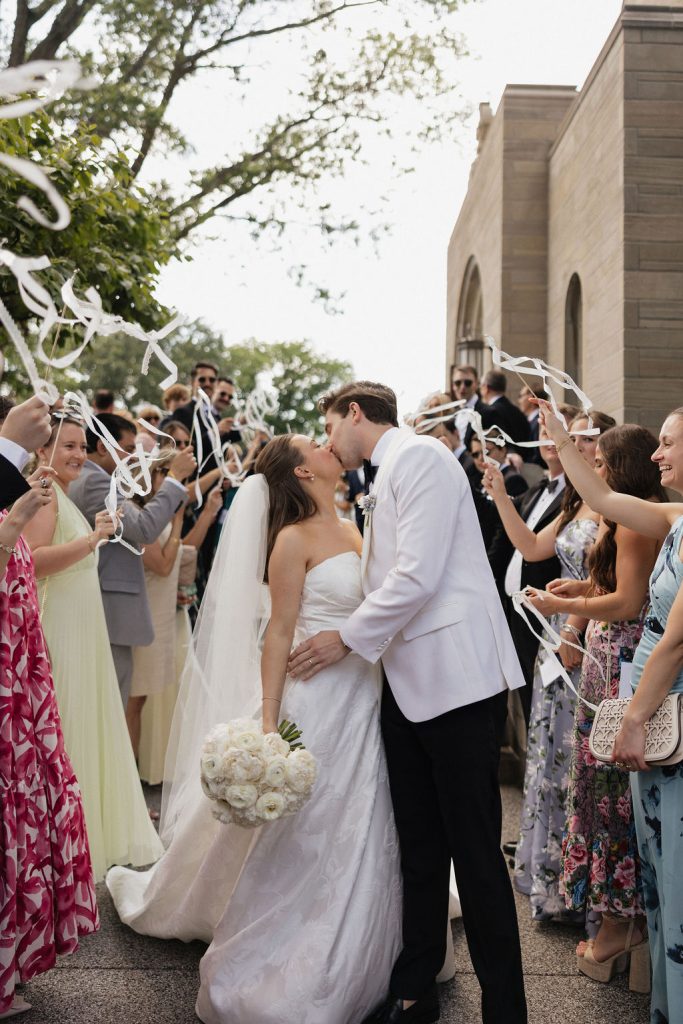 Bride and groom kissing after their wedding ceremony with guests celebrating in the background. Wedding day coordinated by Coordinating with Catherine.