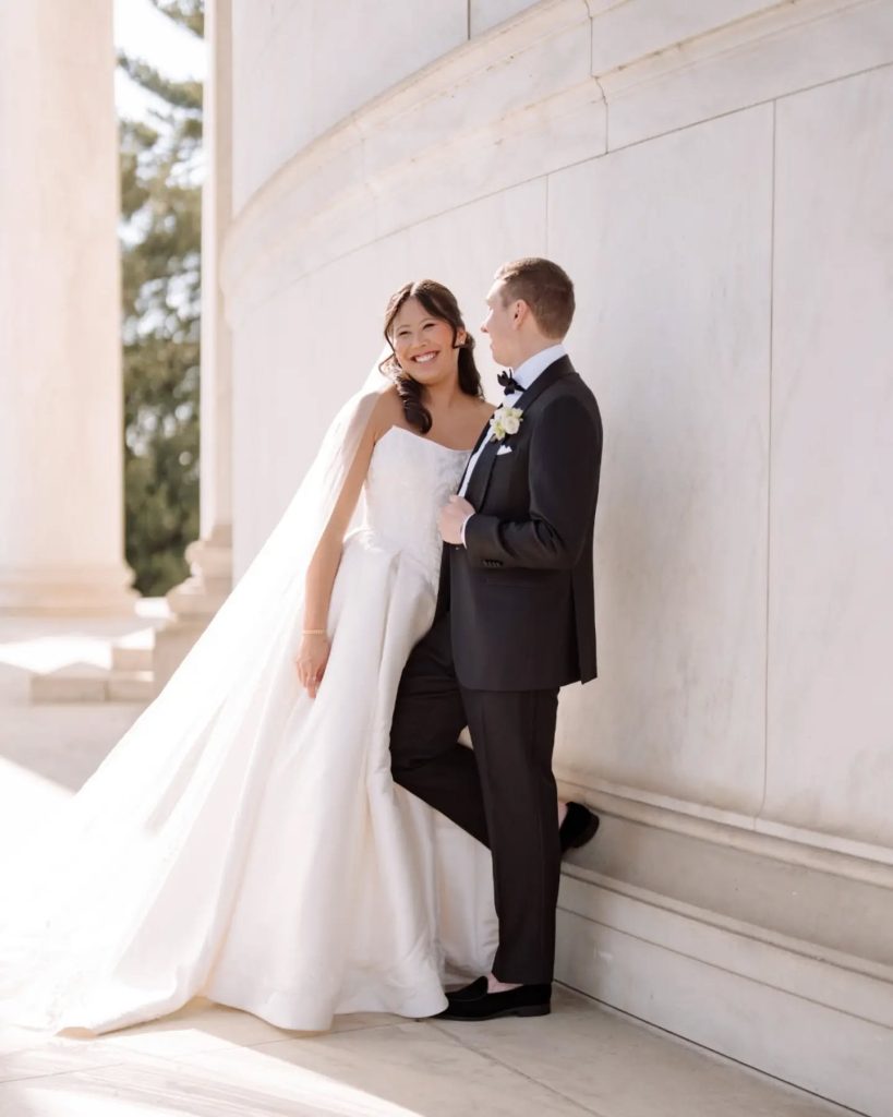 bride and groom leaning against white wall in washington dc during wedding couples portrait session