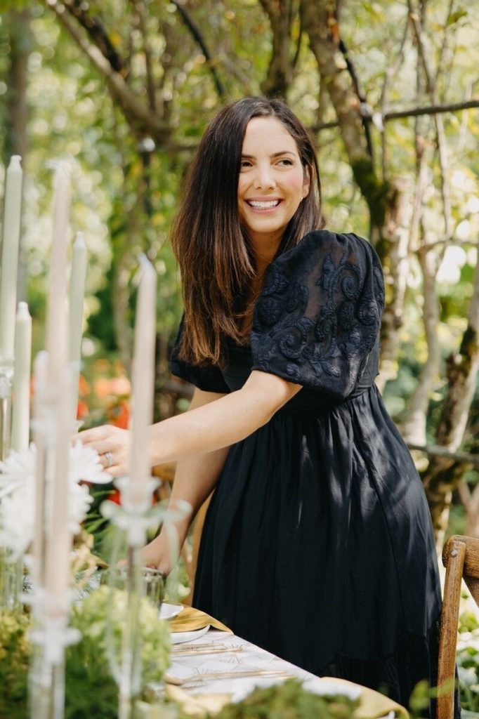 Kristina Conrad, founder of Vowed Weddings, styling an elegant wedding tablescape surrounded by candles, florals, and natural greenery.
