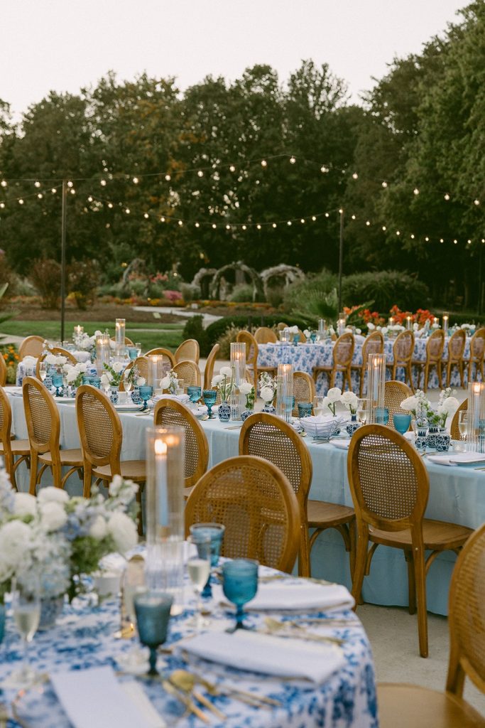 Outdoor wedding reception featuring blue patterned linens, candlelight, and bistro string lights coordinated by Vowed Weddings.