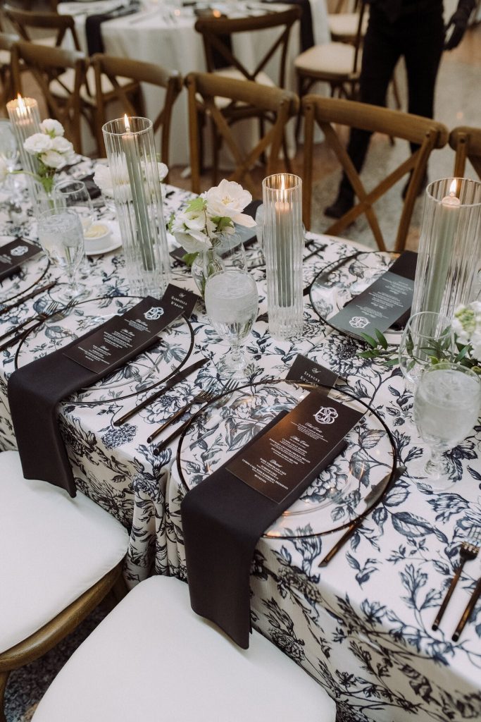 Wedding reception table featuring black and white floral linens, personalized menus, candlelight, and elegant place settings coordinated by Vowed Weddings.
