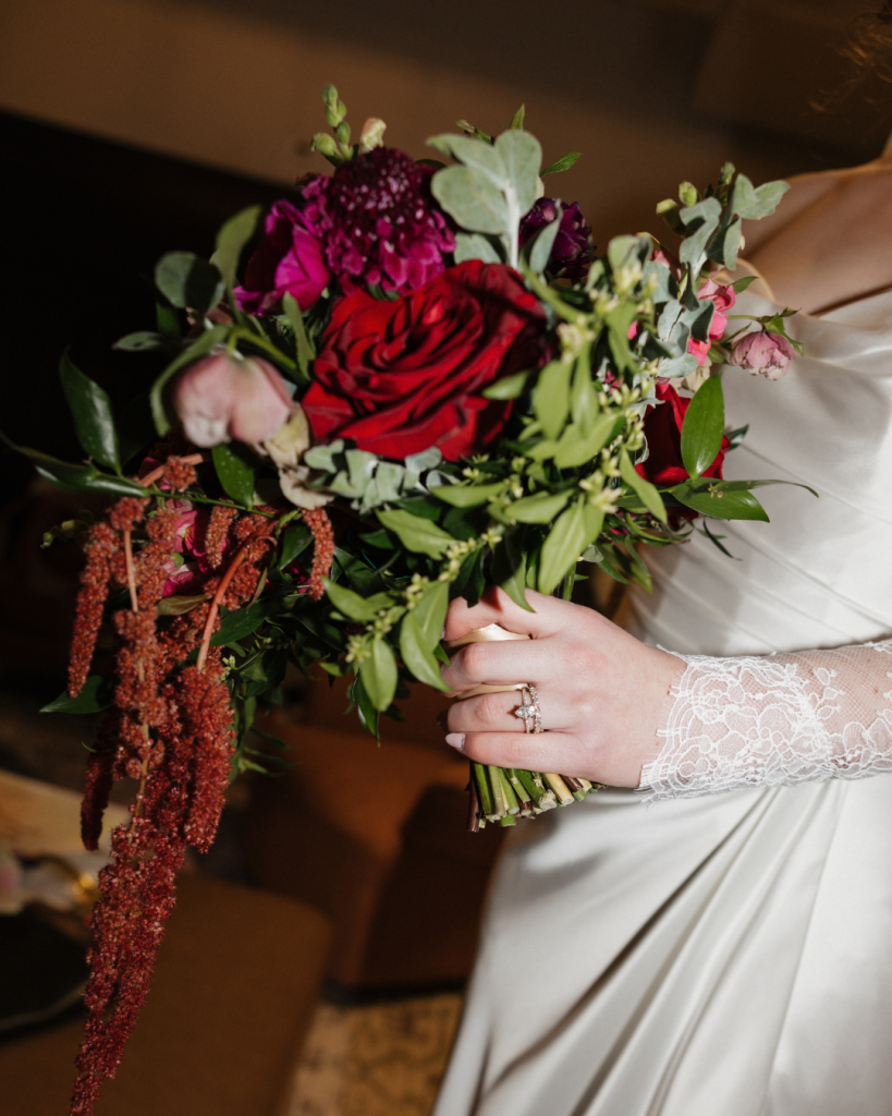 Close view of the bride's colorful bouquet featuring red roses, pink blooms, greenery, and trailing amaranthus.