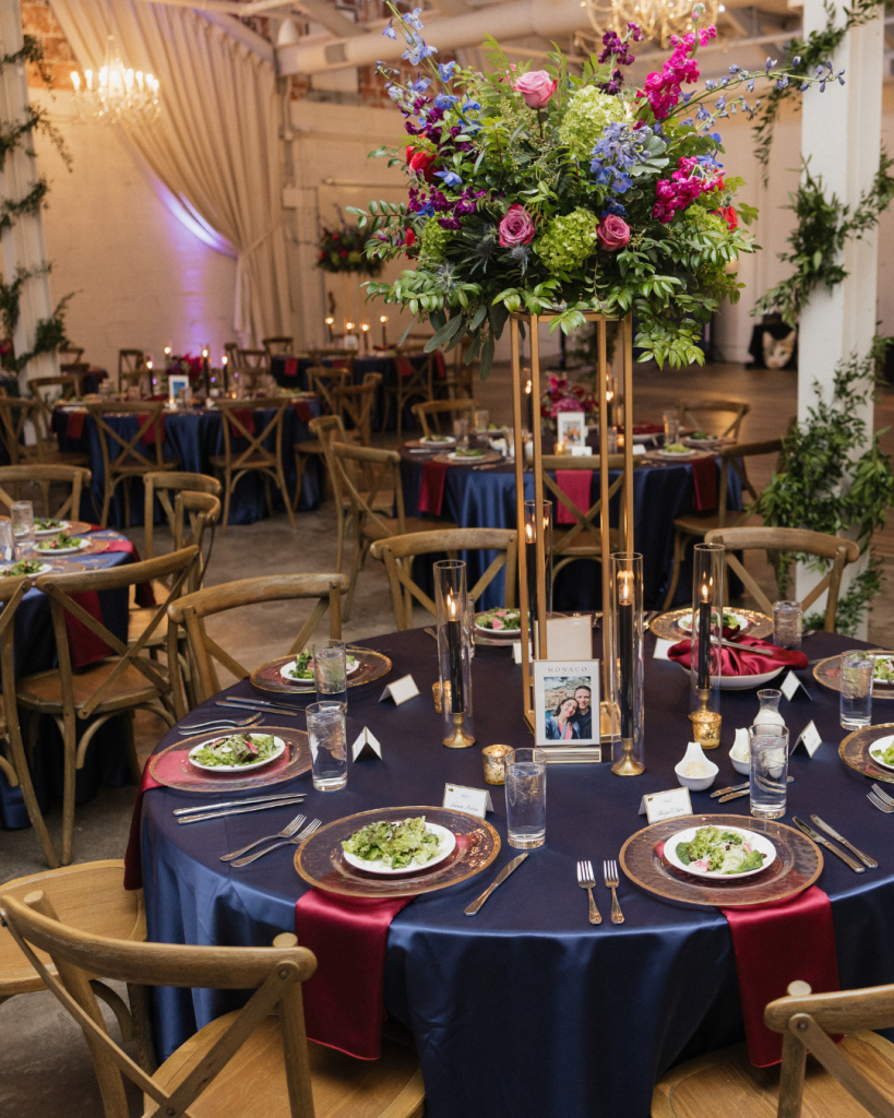 Reception tables at The Casey featuring navy linens, burgundy runners, tall floral centerpieces, candles, and rentals from Curated Events Charlotte.