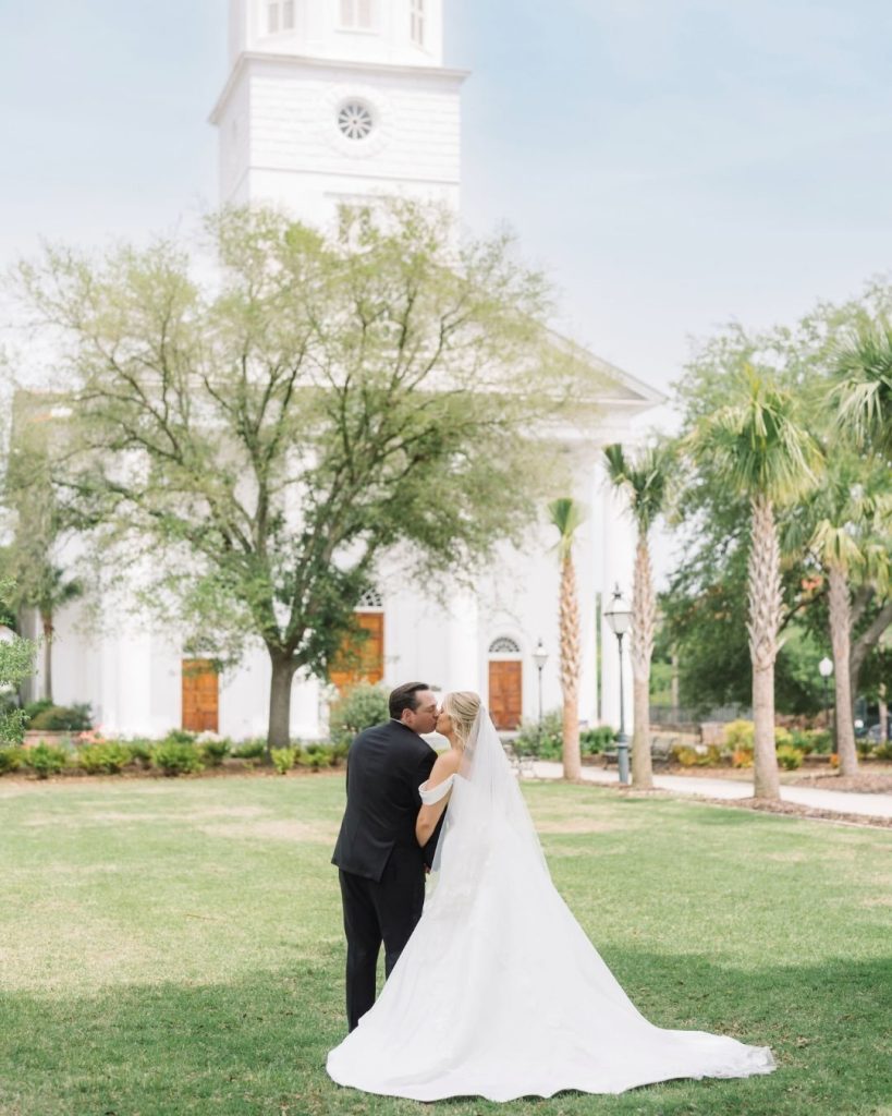 Bride and groom walking hand in hand across a grassy lawn.