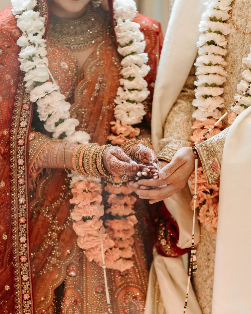 Close-up of the bride and groom's joined, henna-covered hands, layered in white and peach floral garlands