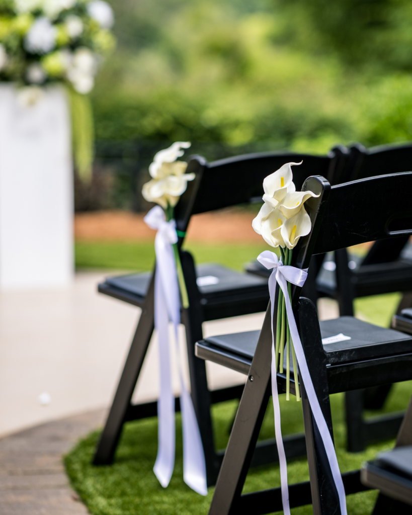 Outdoor ceremony chairs decorated with white calla lilies tied with flowing white ribbon.