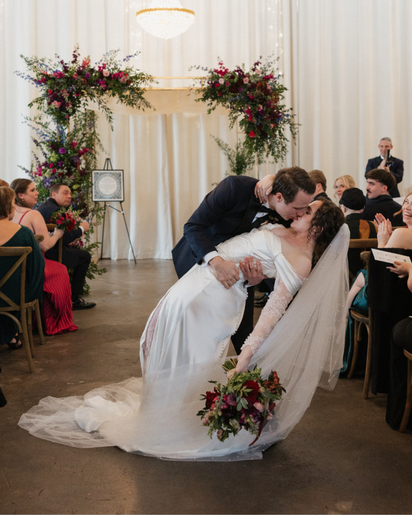 Bride and groom share their first kiss beneath a floral chuppah during a Jewish wedding ceremony at The Casey in Charlotte.